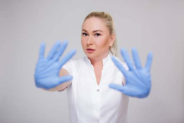 terveydenhuollon ja koronaviruksen pandemian käsite - naislääkärin muotokuva valkoisissa univormuissa ja sinisissä käsineissä, joissa on stop-merkki harmaalla taustalla - Valokuva, kuva