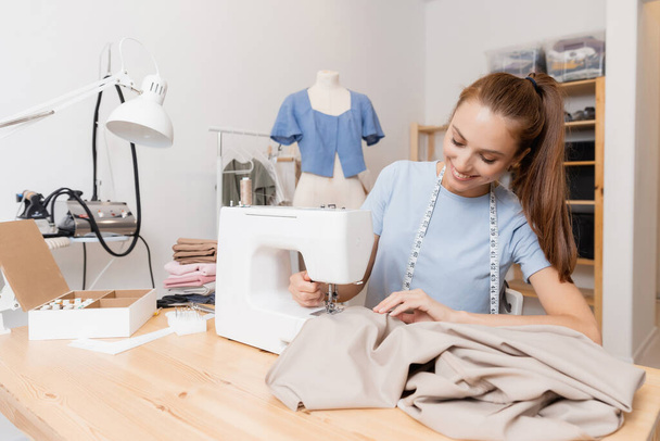 Ευτυχισμένη γυναίκα ράφτης ράφτης λειτουργεί με την προσαρμογή νέα και μοντέρνα ρούχα, ράψτε το χώρο εργασίας - Φωτογραφία, εικόνα