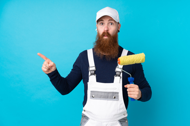 Painter man with long beard over isolated blue background pointing to the laterals having doubts - Photo, Image