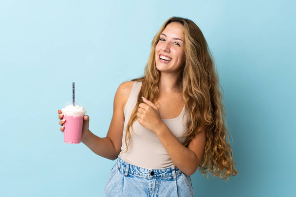 Young woman with strawberry milkshake isolated on blue background celebrating a victory - Fotografie, Obrázek