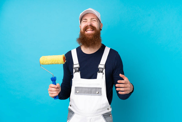 Schilder man met lange baard over geïsoleerde blauwe achtergrond lachen - Foto, afbeelding