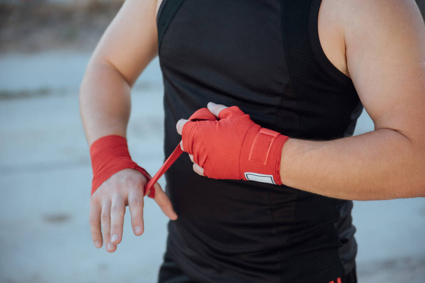 Closeup male hand of boxer with red boxing bandages.Boxing man binds the bandage on his hand, before training, detail photo - Zdjęcie, obraz