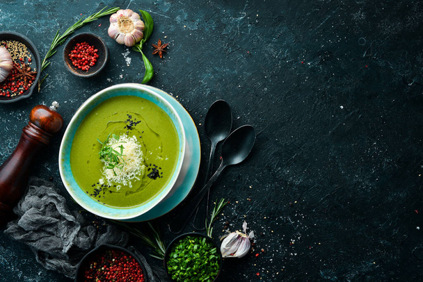 Healthy food. Green soup with broccoli and spinach in a plate on a black stone background. Top view. Rustic style. - 写真・画像