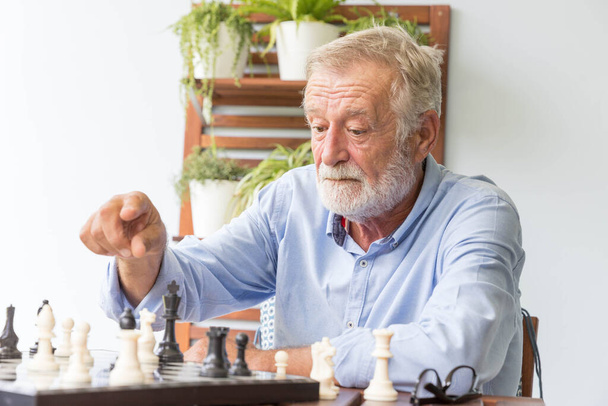 Starszy emeryt gra ze sobą w szachy w domu. - Zdjęcie, obraz