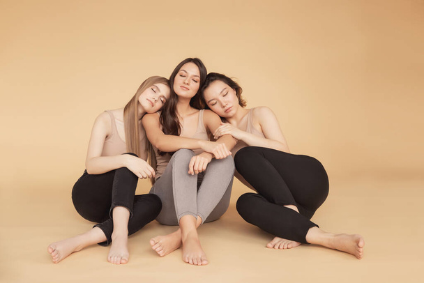 Glückliche junge multikulturelle asiatische Frauen, kaukasische Umarmungen und Lachen im Studio auf beigem Hintergrund. Beauty-Spa-Behandlung Hautpflege-Konzept - Foto, Bild