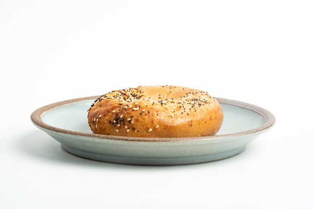 A single freshly baked bagel on a ceramic plate set on a plain white background. - Photo, Image