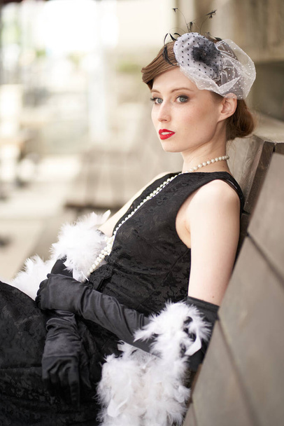 帽子の美しいブルネットの女性、赤い唇の黒いレトロなドレス。座って目を離して                                - 写真・画像