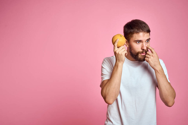 Young man with orange on a pink background in a white t-shirt emotions fun gesticulating with model hands - Photo, Image