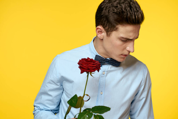 Retrato de un hombre con una rosa roja sobre un fondo amarillo y una camisa ligera pajarita caballero - Foto, imagen
