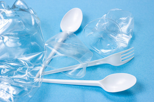 Plastic spoons, forks and cups as a disposable waste with copy space on bright blue background. Environmental pollution and litter recycling concept. - Photo, Image