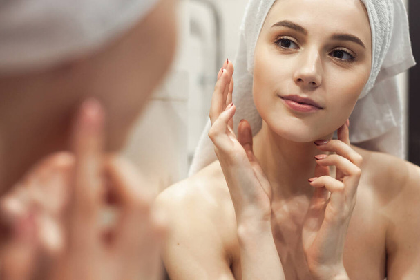 Young woman in bathroom behind mirror. Skincare  treatment concept - Photo, image