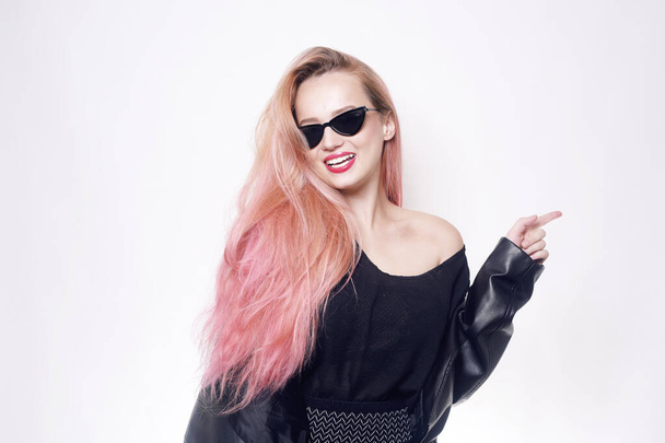 Una chica con el pelo rosa en gafas y ropa negra muestra un espacio vacío para el texto o un producto. Viernes Negro. Mujer sonriendo - Foto, Imagen