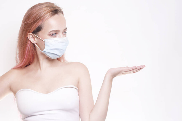 Mädchen mit rosa Haaren in einer Maske. Frau in medizinischer Maske zeigt Leerstelle für Text - Foto, Bild