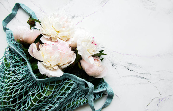 Pink peony in string bag  on white marble background. Flat lay - Photo, Image