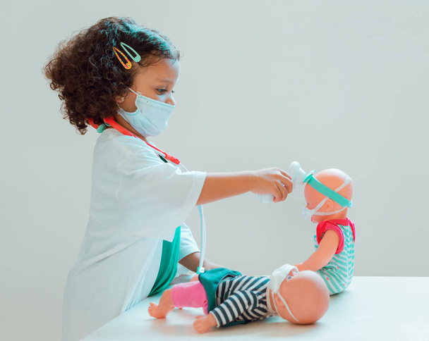 Een klein meisje dat doktertje speelt meet de koorts van haar patiënt, iedereen draagt beschermende maskers - Foto, afbeelding
