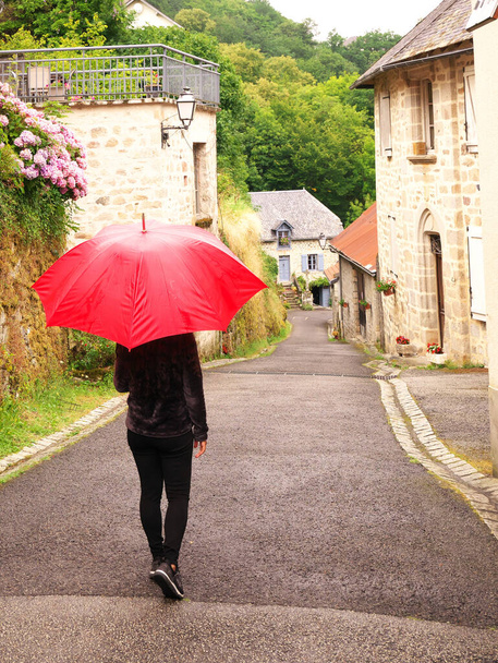 Una mujer camina por un pueblo con un paraguas rojo - Foto, Imagen