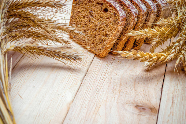 Pan integral de trigo. Hoja fresca de pan rústico tradicional con espiga de trigo o espiga sobre fondo de textura de madera. Panadería de centeno con pan crujiente y migas. Hornear en casa - Foto, Imagen