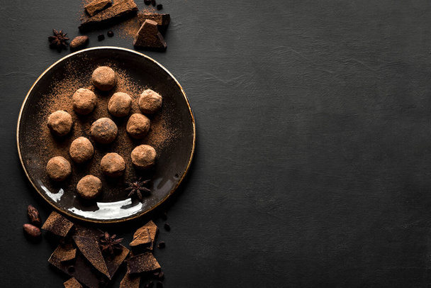 Σπιτικές τρούφες σοκολάτας σε πιάτο και κομμάτια σοκολάτας σε μαύρο, top view, αντιγραφή χώρου. - Φωτογραφία, εικόνα