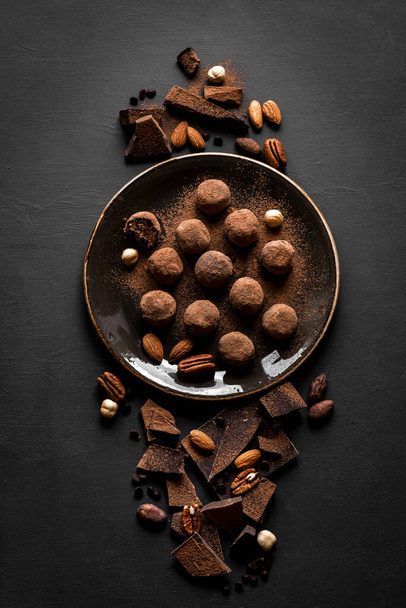 Chocolate truffles with dark chocolate and nuts on black background, top view, copy space. Vegan homemade chocolate energy balls or truffles for dessert. - Φωτογραφία, εικόνα