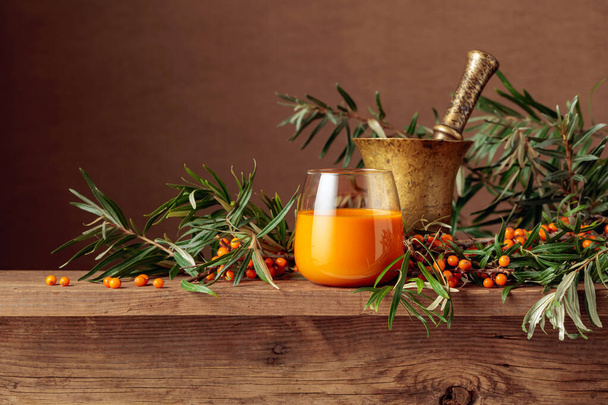 A glass of sea buckthorn juice with fresh berries on an old wooden table. A healthy vitamin drink.  - Photo, Image
