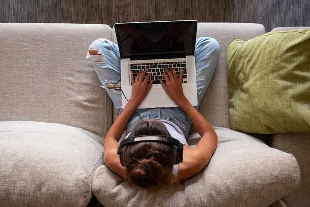 felső kilátás fiatal lány dolgozik egy laptop és zenét hallgatni ül a kanapén otthon - Fotó, kép