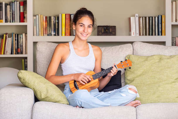 young girl playing ukulele sitting in a sofa at home - Foto, Bild
