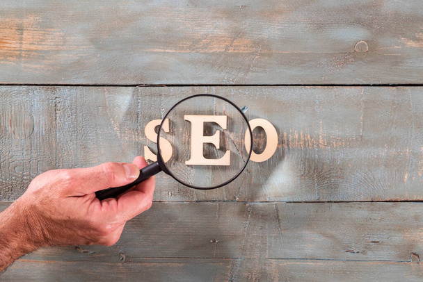 man looking through magnifying glass a seo word formed with white letters. Search engine optimization concept. - Фото, зображення
