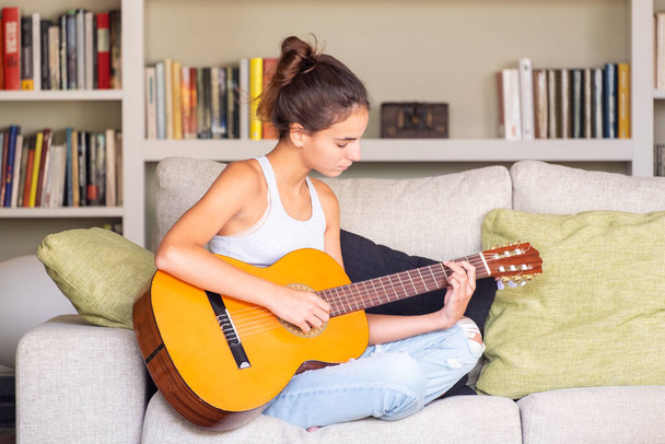 young girl playing guitar sitting in a sofa at home - Valokuva, kuva