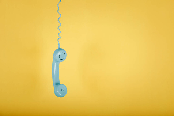 blue vintage telephone hanging on yellow background - Фото, изображение