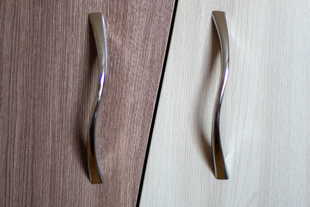 Twee metalen meubelgrepen op een bruin-witte deur. - Foto, afbeelding