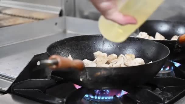 Close-up van een mannelijke chef-kok giet olie op een koekenpan die staat op het fornuis in een professionele keuken in een restaurant, het proces van koken in een restaurant. - Video