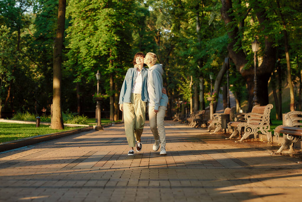 Full length shot of happy lesbian couple having a date in the city park, two girls spending time together, kissing while walking outdoors - Foto, afbeelding