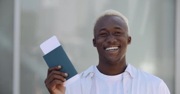 Jeune étudiant afro-américain attrayant en vêtements blancs sourit toothy, ouvre joyeusement sa bouche crie de bonheur, montre des billets d'avion de voyage et passeport à la caméra, célèbre les vacances - Séquence, vidéo