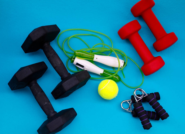 Oefenmateriaal. Gewichten, springtouw, tennisbal, handgreep versterker op een blauwe mat. - Foto, afbeelding