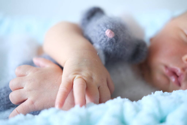 Un bebé recién nacido dormido se encuentra en una manta azul, un ratón de juguete de ganchillo en las manos de los bebés  - Foto, Imagen