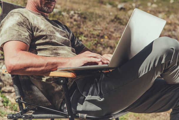 Kaukasische Männer in den Vierzigern, die von ihrem Laptop aus ferngesteuert arbeiten, während sie draußen bleiben. Thema Drahtlostechnologie. - Foto, Bild