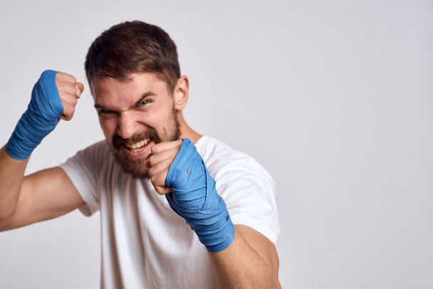 Sportowy mężczyzna w białej koszulce z bandażami bokserskimi na rękach ćwiczący ćwiczenia uderzeniowe poprawiające umiejętności - Zdjęcie, obraz