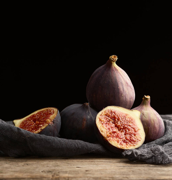 ripe whole and halved purple figs on a black napkin, low key, close up - Photo, Image