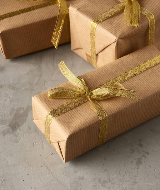 caja rectangular envuelta en papel marrón y atada con una cinta de seda con un lazo, regalo sobre un fondo gris, primer plano - Foto, imagen