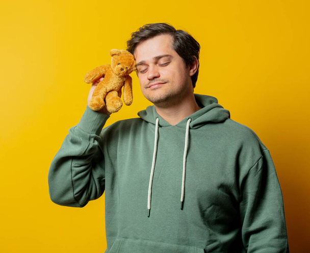 Guy in groene hoodie met teddybeer op gele achtergrond - Foto, afbeelding