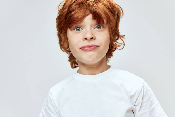 Red-haired boy grimaces close-up white t-shirt studio emotions  - Fotó, kép