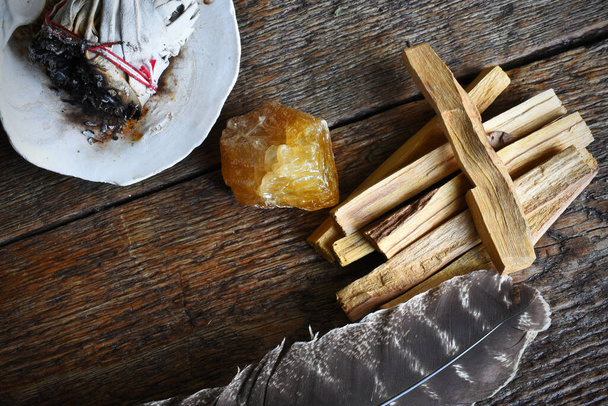 暗い木製のテーブルの上に蜂蜜の方解石の結晶と神聖な羽でパロ・サント・スマッジの棒のトップビューの画像.  - 写真・画像