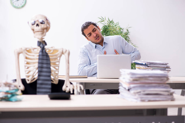 Fiatal férfi alkalmazott és csontváz az irodában - Fotó, kép
