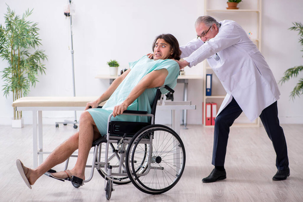 Jovem paciente do sexo masculino em cadeira de rodas e médico traumatologista experiente - Foto, Imagem