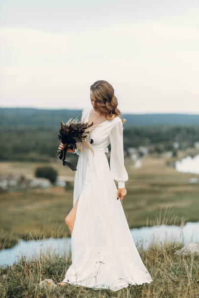 Bride with a bouquet of dried flowers walking in nature. Boho style wedding in autumn. - Фото, изображение