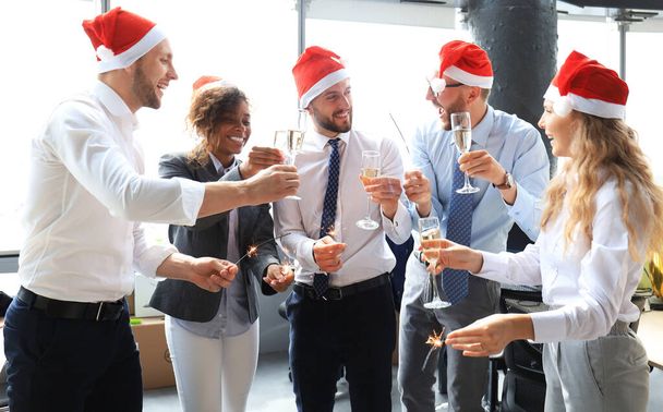 Young business partners are lighting bengal lights and drinking champagne in a modern office. Merry Christmas and Happy New Year. - Φωτογραφία, εικόνα