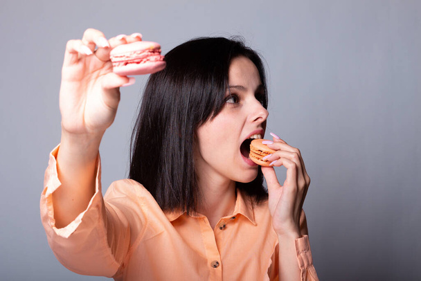 woman in orange shirt holds macaroon cookies in hand - Фото, зображення