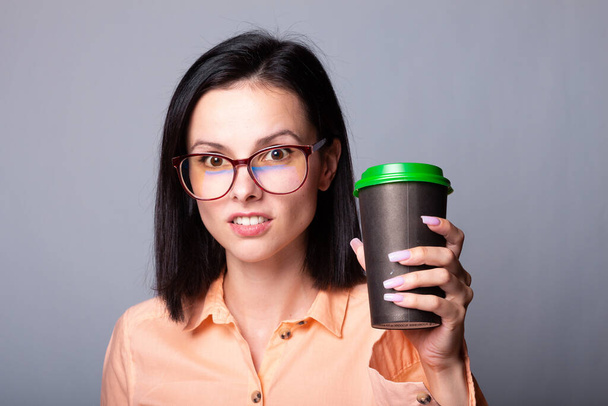 donna in camicia arancione e bicchieri che tiene in mano una tazza di caffè, sfondo grigio - Foto, immagini