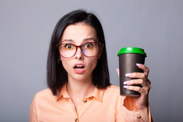 cute girl in an orange shirt holds a cup of coffee in her hands, gray background - Foto, immagini