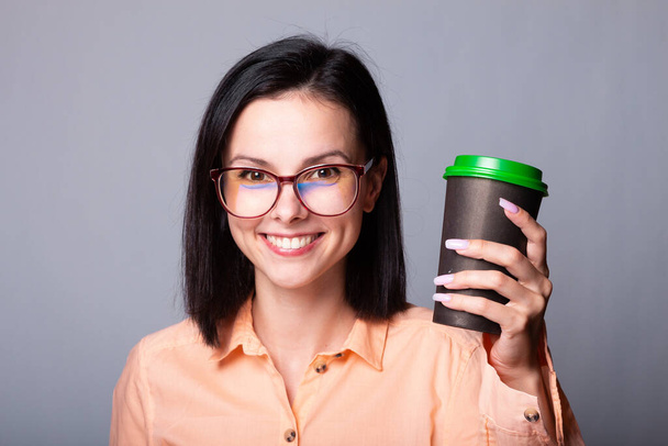 cute girl in an orange shirt holds a cup of coffee in her hands, gray background - Foto, imagen
